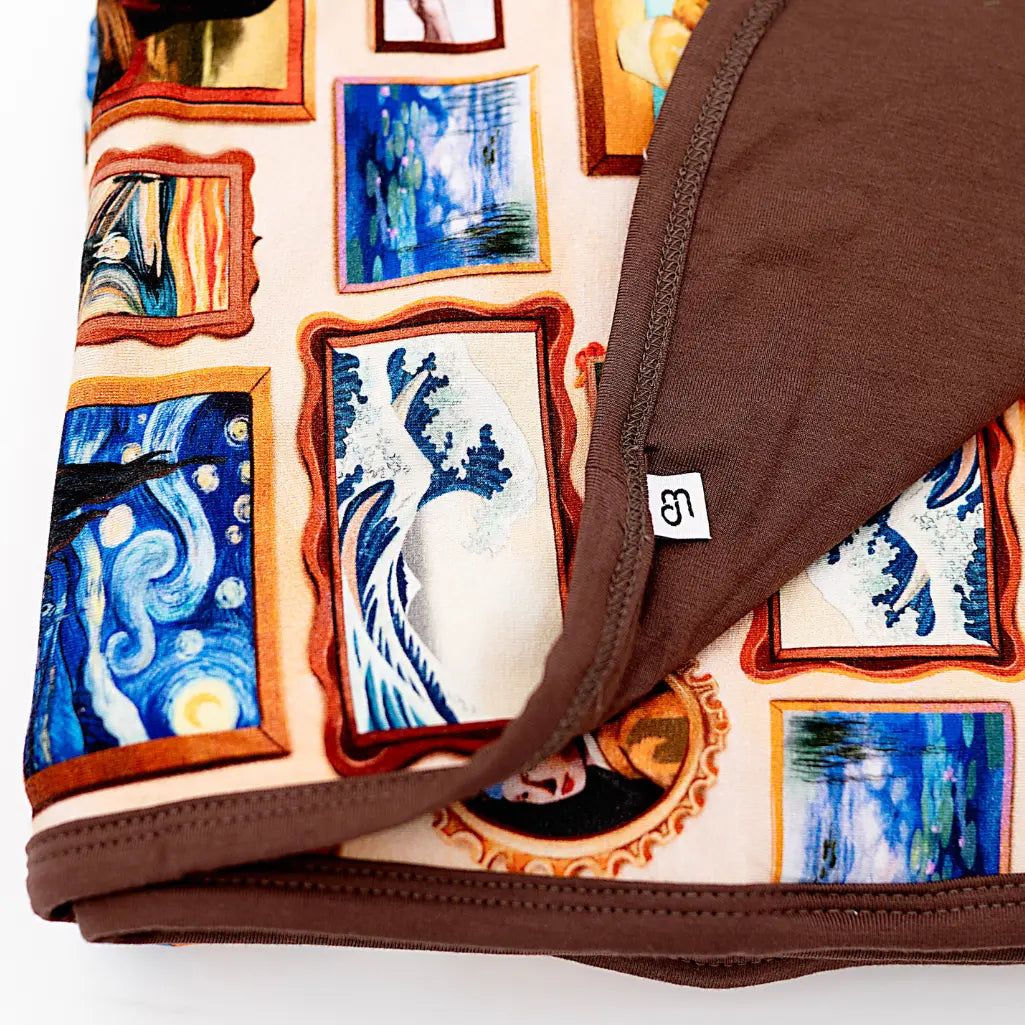 Close-up of a folded double-layered blanket with a framed classic paintings print on one side and solid brown on the other.